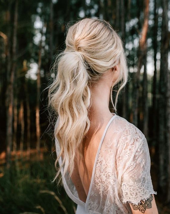 bridal hairstyle idea on blonde hair with ponytail and beach waves and loose hair strands around the face.
