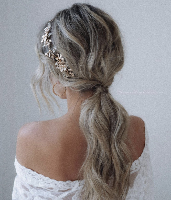 elegant bridal hairstyle with low ponytail and soft waves, adorned by a stunning gold hairpiece.