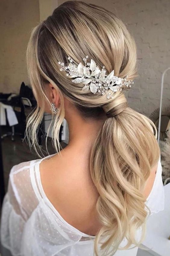 beautiful bridal hairstyle on blonde hair with low ponytail and soft waves, adorned by a stunning gold hairpiece.