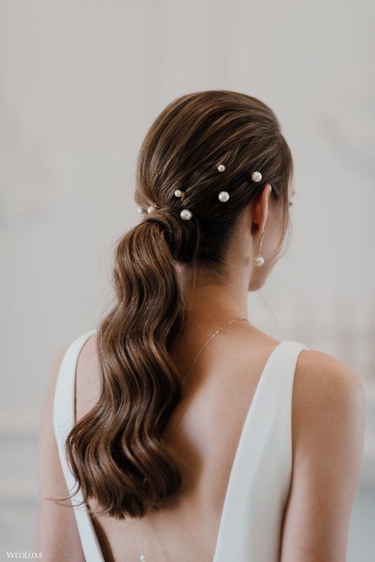 minimalist and elegant bridal hairstyle on brunette hair with a low ponytail, wavy hair and small pearls.