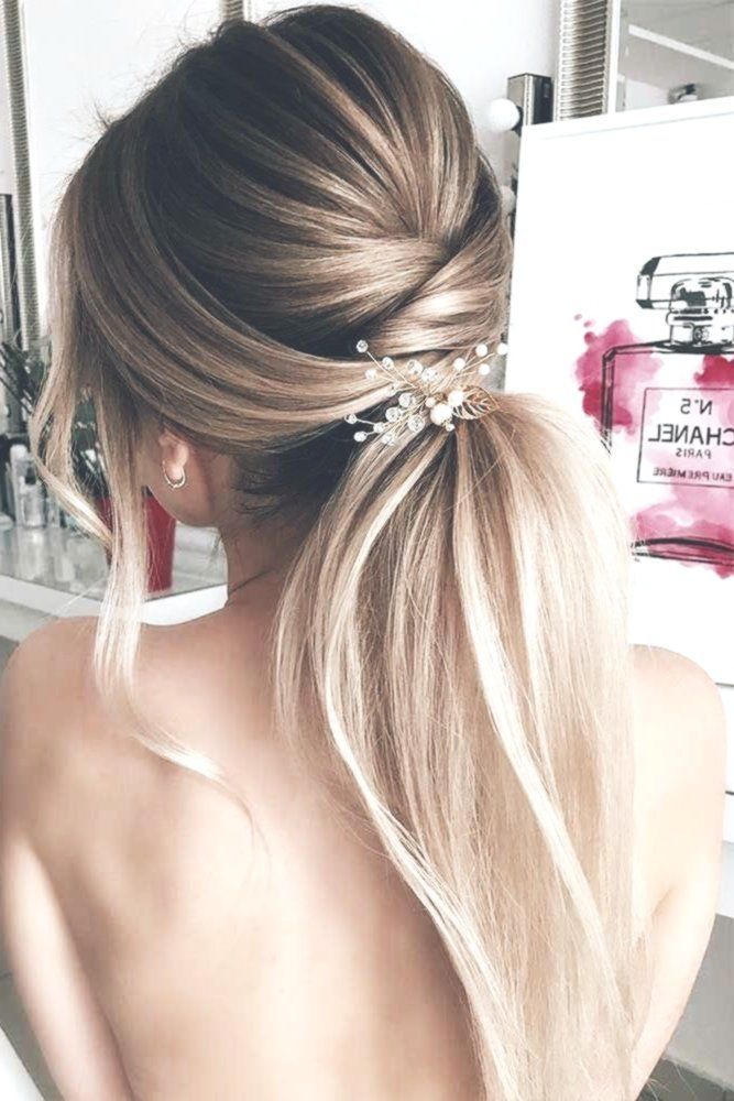 chic bridal hairstyle idea on blonde hair with a twisted low ponytail and loose strands around the face, embellished with delicate gold hairpiece