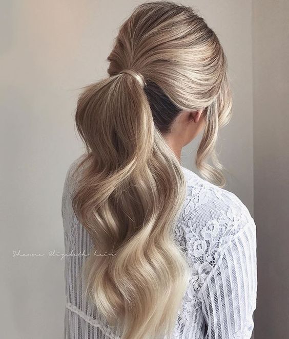 bridal hairstyle idea on blonde hair with ponytail and soft waves, with loose hair strands around the face.
