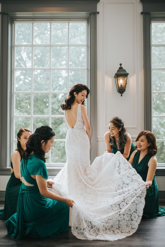 bridesmaids wearing emerald color dress holding the bride dress skirt