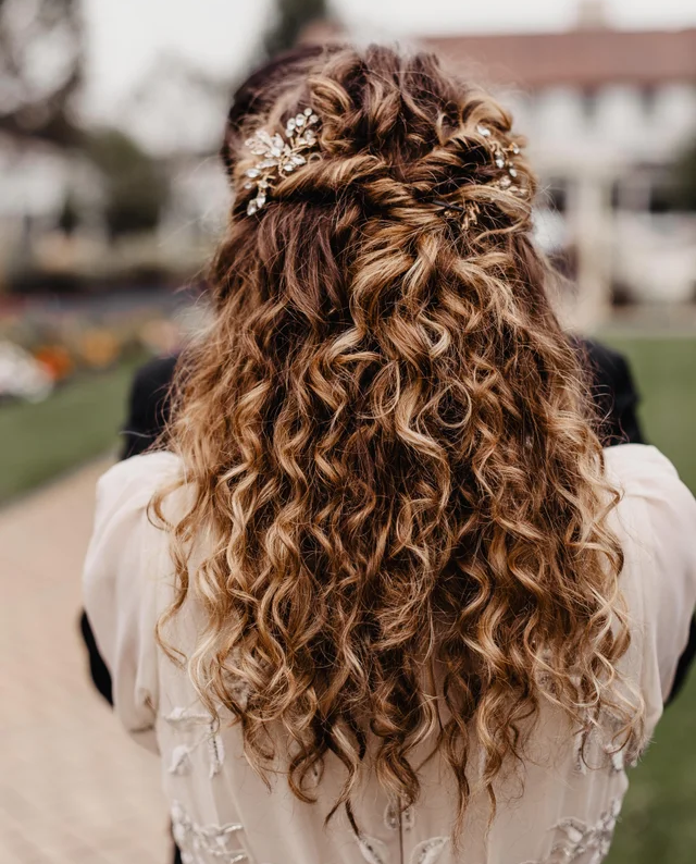 Blonde bride with curly hair styled half up half down, using hair accessories