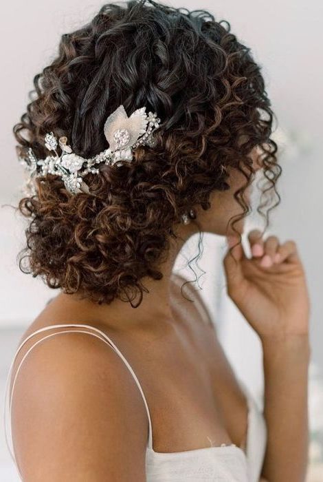 brunette bride wearing her curly hair in a low bun with floral hair accessory