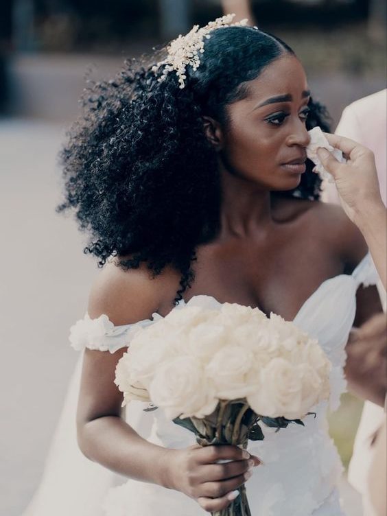 Black bride with natural hair styled down with a mid part and voluminous curls, with a headpiece on top