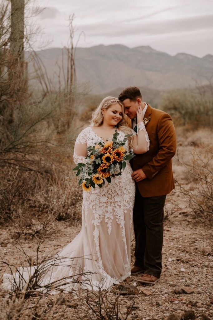 Bride and groom portrait, bride uses a long sleeve lace wedding dress and holds a sunflower wedding bouquet and the groom uses a brown velvet suit